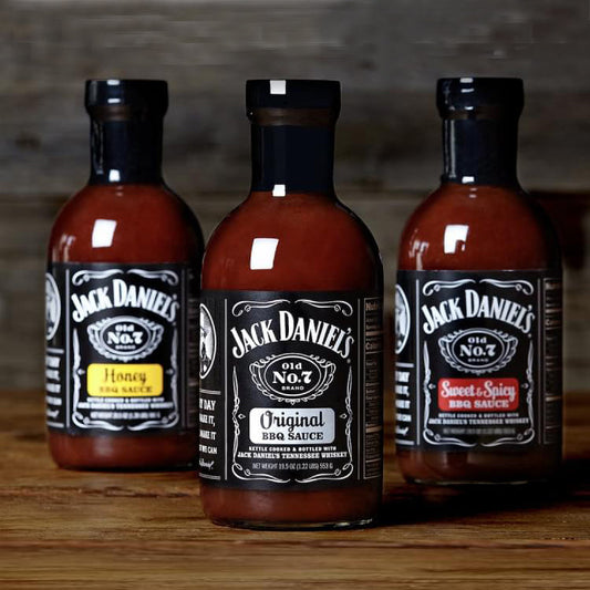 Three bottles of Jack Daniel's BBQ sauce—Original, Honey, and Sweet & Spicy—on wooden surface.