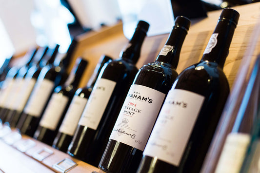 Close-up of vintage port wine bottles displayed on a wooden shelf, wine store setting