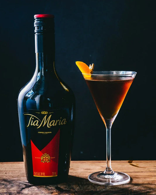 Tia Maria coffee liqueur bottle beside a coffee cocktail with orange twist garnish